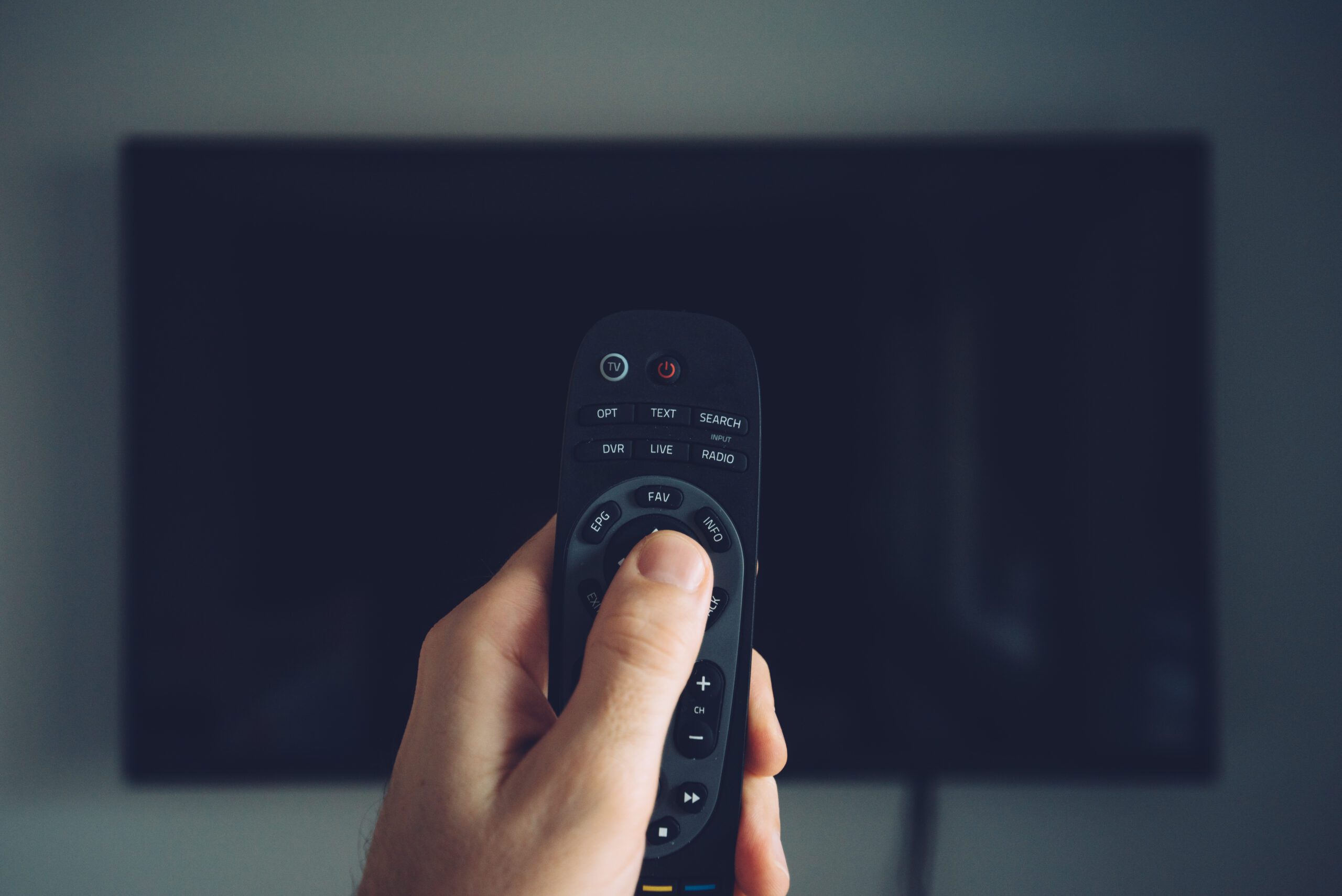 Man holding tv remote in front of a tv. How to Reset a FireStick Remote