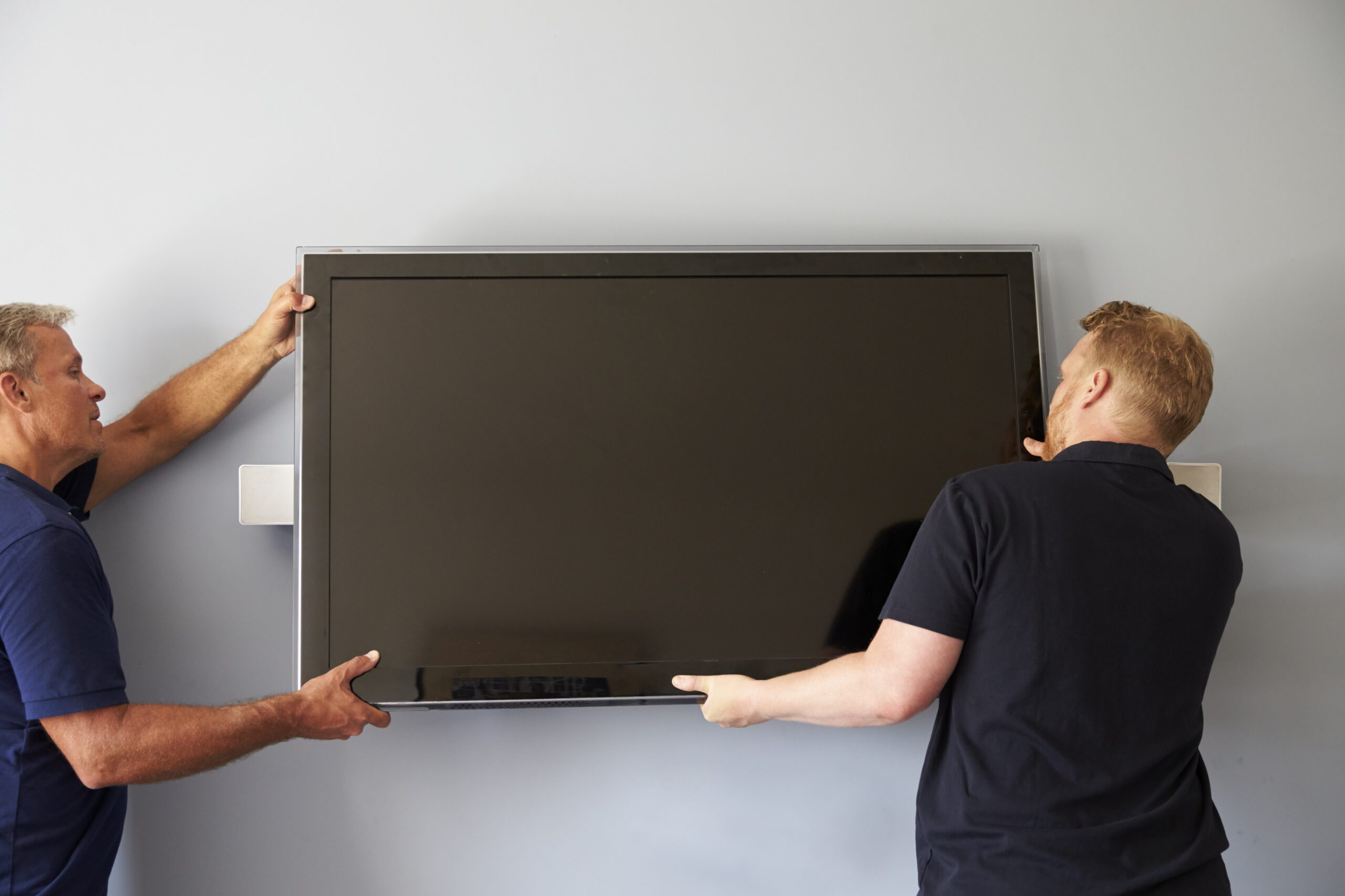 two men lifting a tv based on how high it should be mounted