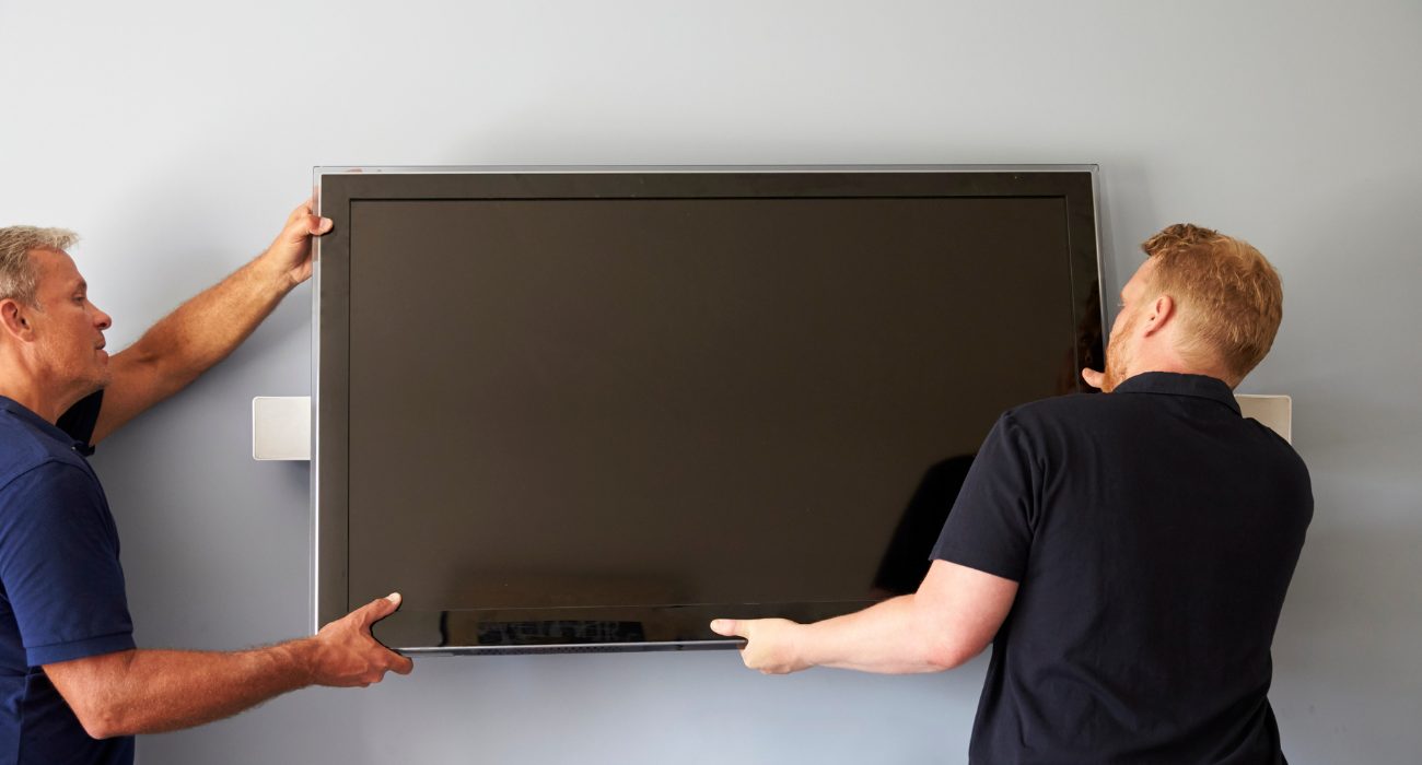 Two people carefully lifting a TV onto a wall mount